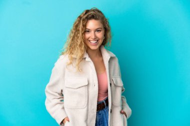 Genç sarışın kadın mavi arka planda yalnız gülüyor.