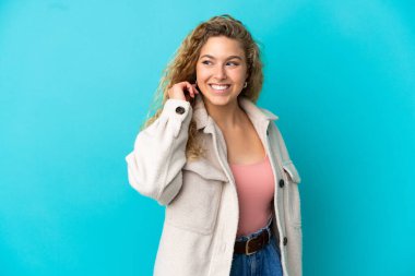 Genç sarışın kadın mavi arka planda yalnız gülüyor.