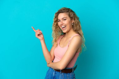 Mavi arka planda izole edilmiş genç sarışın kadın parmağını yana doğru gösteriyor.