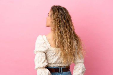 Genç sarışın kadın pembe arka planda izole edilmiş ve arkasına bakıyor.