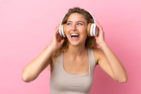 Young blonde woman isolated on pink background listening music and singing