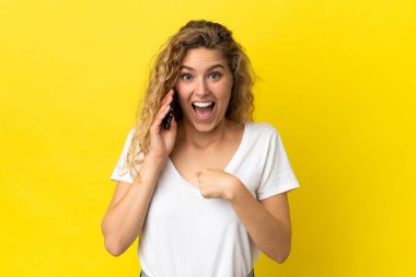 Sarı arka planda izole edilmiş cep telefonu kullanan genç sarışın kadın.