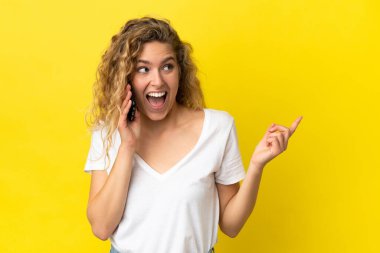 Sarı arka planda izole edilmiş cep telefonu kullanan genç sarışın kadın bir parmağını kaldırarak çözümü bulmayı umuyor.