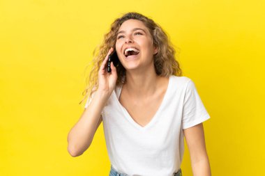 Sarı arka planda izole edilmiş cep telefonu kullanan genç sarışın kadın gülüyor.