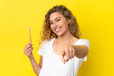 Sarı arka planda dişlerini fırçalayan beyaz bir kadın mutlu bir ifadeyle önünü işaret ediyor.