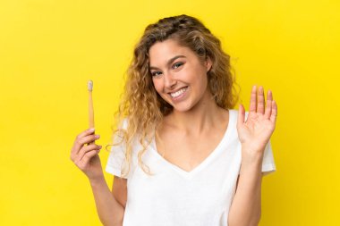 Sarı arka planda dişlerini fırçalayan beyaz bir kadın mutlu bir ifadeyle selamlıyor.