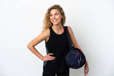 Spor çantalı genç bayan beyaz arka planda izole edilmiş kolları kalçasında poz veriyor ve gülümsüyor