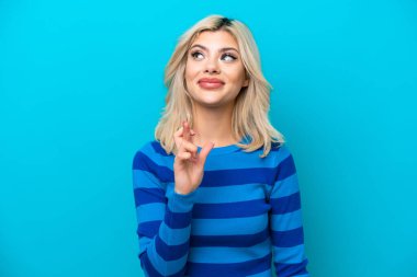 Genç Rus kadın mavi arka planda izole edilmiş, şans diliyor ve en iyisini diliyor.