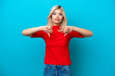 Mavi arka planda izole edilmiş genç bir Rus kadın baş parmağını iki eliyle aşağı gösteriyor.