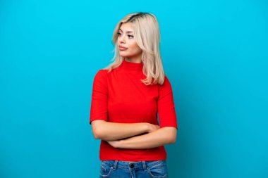 Mavi arka planda izole edilmiş genç Rus kadın kollarını çapraz tutuyor.