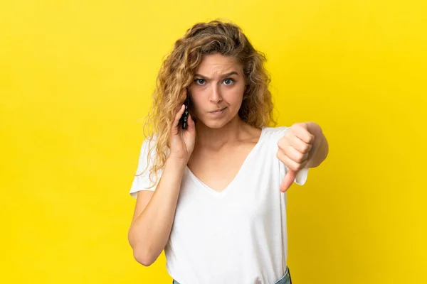 年轻的金发女子使用黄色背景的手机 带着负面表情垂下大拇指 — 图库照片