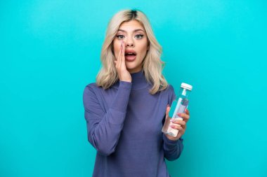 Mavi arka planda bir şişe suyu olan genç bir Rus kadın şaşırmış ve şok olmuş bir yüz ifadesi var.