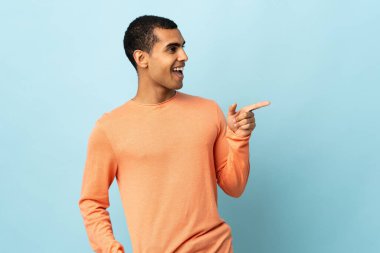 İzole edilmiş arka planda yaşayan Afro-Amerikalı bir adam parmağını yana uzatıp bir ürün sunuyor.