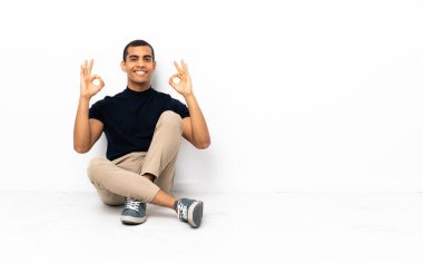 Afro-Amerikalı bir adam yerde oturmuş parmaklarıyla 