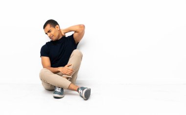 Afro-Amerikalı bir adam yerde boynu ağrıyarak oturuyor.