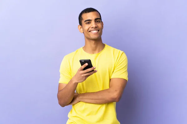 Hombre Afroamericano Sobre Fondo Púrpura Aislado Usando Teléfono Móvil Riendo —  Fotos de Stock