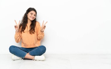 Genç Rus kız yerde oturuyor ve iki eliyle zafer işareti gösteriyor.