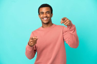 İzole edilmiş mavi arka planda Afro-Amerikalı yakışıklı adam mutlu bir ifadeyle öne bakıyor.