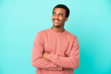 İzole edilmiş mavi arka planda Afro-Amerikalı yakışıklı bir adam bir fikir ararken düşünüyor.