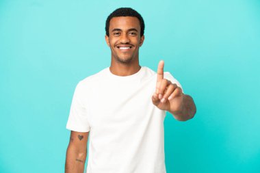 İzole edilmiş mavi arka planda Afro-Amerikalı yakışıklı bir adam parmağını kaldırıyor ve gösteriyor.