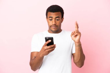 İzole edilmiş pembe arka planda, parmakları çapraz cep telefonu kullanan Afro-Amerikalı yakışıklı bir adam.