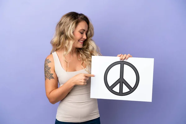 紫の背景に平和のシンボルを持つプラカードを保持し それを指す若いブラジル人女性 — ストック写真