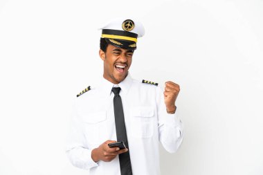 Afro-Amerikan uçak pilotu izole edilmiş beyaz arka planda ve telefon zafer pozisyonunda.