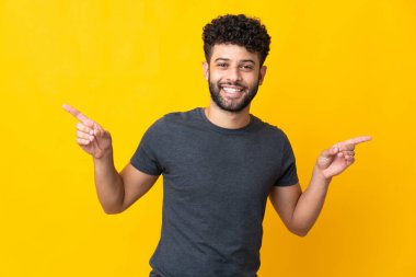 Sarı arka planda izole edilmiş genç Faslı adam parmak uçlarında ve mutlu.
