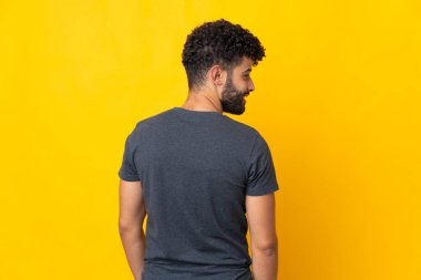 Genç Faslı adam sarı arka planda izole edilmiş. Arka tarafta ve yan tarafa bakıyor.
