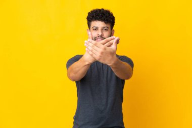 Genç Faslı bir adam sarı arka planda izole edilmiş bir şekilde bir eylemi durdurmak için el hareketi yapıyor.