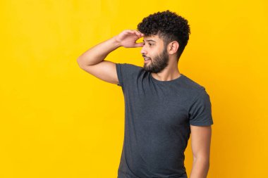 Faslı genç bir adam, sarı arka planda yalıtılmış, sürpriz bir ifadeyle yan tarafa bakarken...