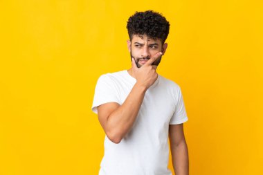 Sarı arka planda izole edilmiş genç Faslı adamın şüpheleri ve şaşkın bir yüz ifadesi var.