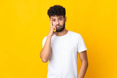 Genç Faslı bir adam sarı arka planda izole edilmiş bir fikir düşünüyor.