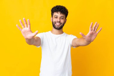 Sarı arka planda izole genç Faslı adam parmaklarıyla ona kadar sayıyor.