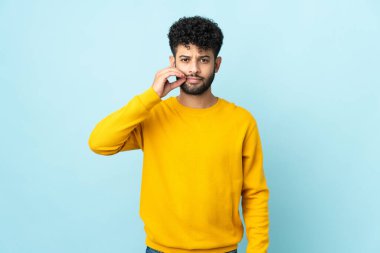 Mavi arka planda izole edilmiş genç Faslı bir adam sessizlik işareti gösteriyor.
