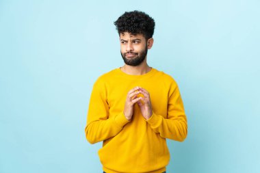 Genç Faslı bir adam mavi arka planda bir şeyler planlıyor.