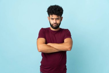 Faslı genç bir adam mutsuz bir ifadeyle mavi arka planda izole edilmiş.