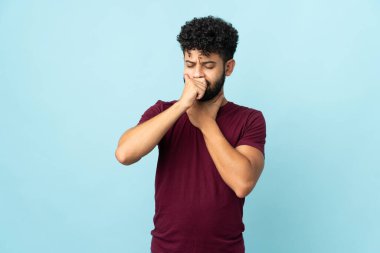 Faslı genç bir adam mavi arka planda çok öksürüyor.