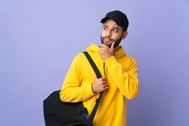 Spor çantalı genç Faslı adam mor arka planda izole edilmiş ve yukarı bakıyor.