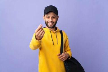 Spor çantalı genç Faslı adam mor arka planda izole edilmiş para hareketi yapıyor.