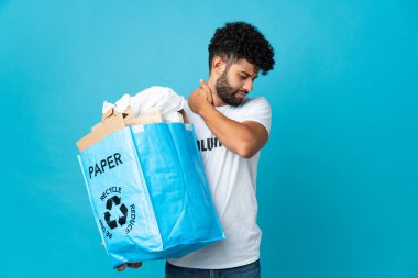 Genç Faslı bir adam, izole bir arka plan üzerinde geri dönüşüm yapmak için bir çanta dolusu kağıt taşıyor. Omuz ağrısı çekiyor.