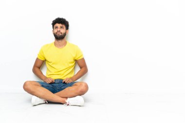 Genç Faslı yakışıklı adam izole edilmiş arka planda yerde oturuyor ve yukarı bakıyor.