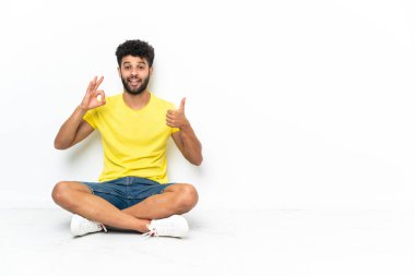 Genç Faslı yakışıklı adam izole bir zeminde oturmuş işaret veriyor ve işaret veriyor.