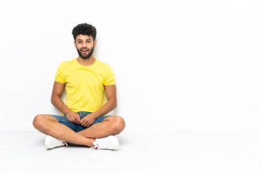 Genç Faslı yakışıklı bir adam yerde izole edilmiş bir şekilde oturuyor ve yüzünde sürpriz bir ifade var.