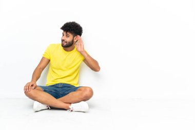 Genç Faslı yakışıklı adam izole bir zeminde oturuyor ve kulağına bir şeyler dinliyor.