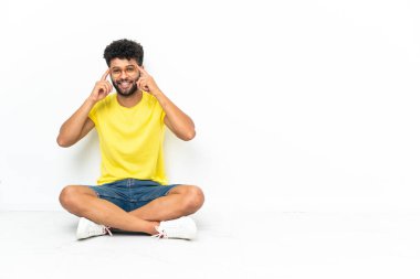 Genç Faslı yakışıklı, gözlüklü ve şaşırmış bir şekilde izole bir zeminde oturuyor.