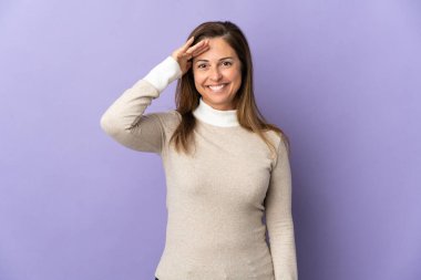 Orta yaşlı Brezilyalı kadın, mor arka planda izole edilmiş, mutlu bir ifadeyle selam veriyor.