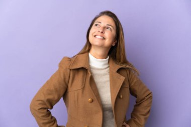 Mor arka planda izole edilmiş orta yaşlı Brezilyalı kadın kolları kalçasında poz veriyor ve gülümsüyor