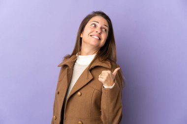 Mor arka planda izole edilmiş orta yaşlı Brezilyalı kadın bir ürünü sunmak için kenarı işaret ediyor.