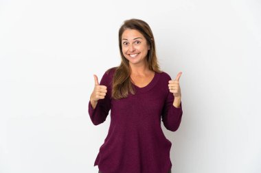 Orta yaşlı Brezilyalı bir kadın beyaz arka planda izole edilmiş. Baş parmakları havada ve gülümsüyor.